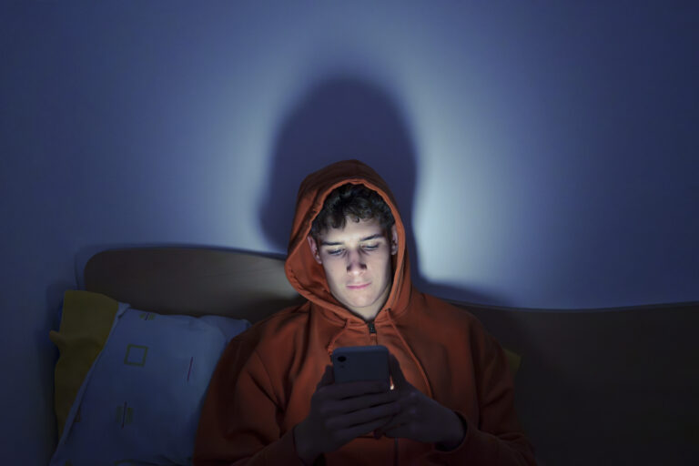 Teenager using smartphone sitting on bed at night