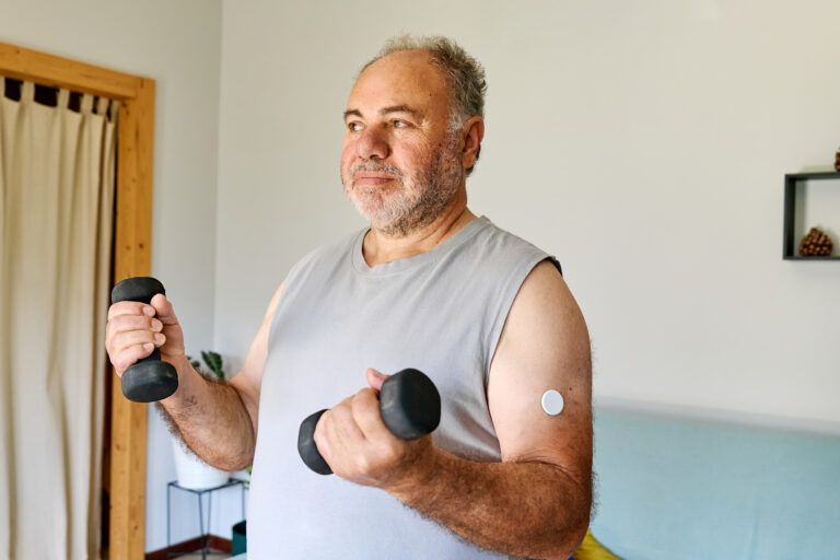 Mature man with diabetes and continuous glucose monitor on his arm making sport exercises at home