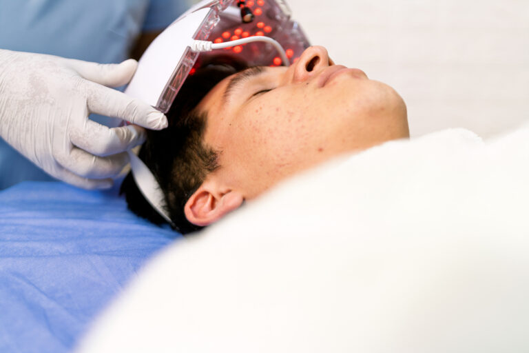 Beautician placing led light therapy mask on young man's face