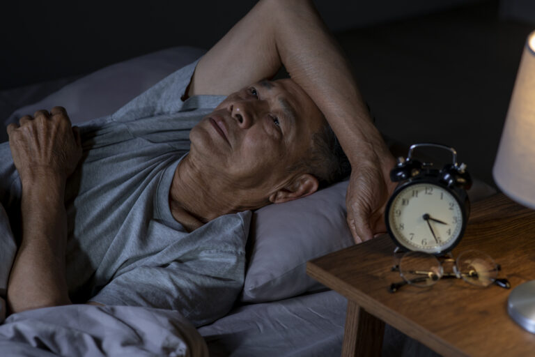 Depressed senior Asian man lying in bed cannot sleep from insomnia