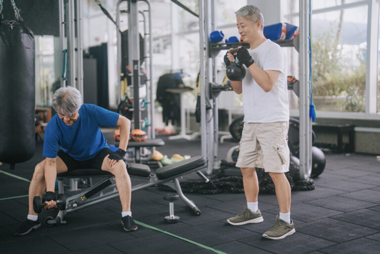 2 active Chinese senior men workout in gym with kettlebell and dumbbell strength training