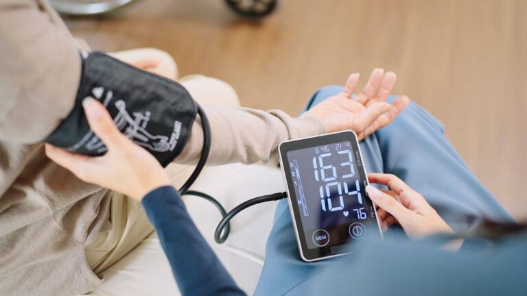 Close up woman caregiver nurse wearing blue scrubs checks blood pressure monitor and heart rate monitor with digital pressure gauge to elderly woman retirement  sitting on bed in bedroom,healthcare setting medical health care plan