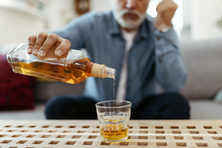 Bottle With Glass of Whiskey on Table and Drunk Man