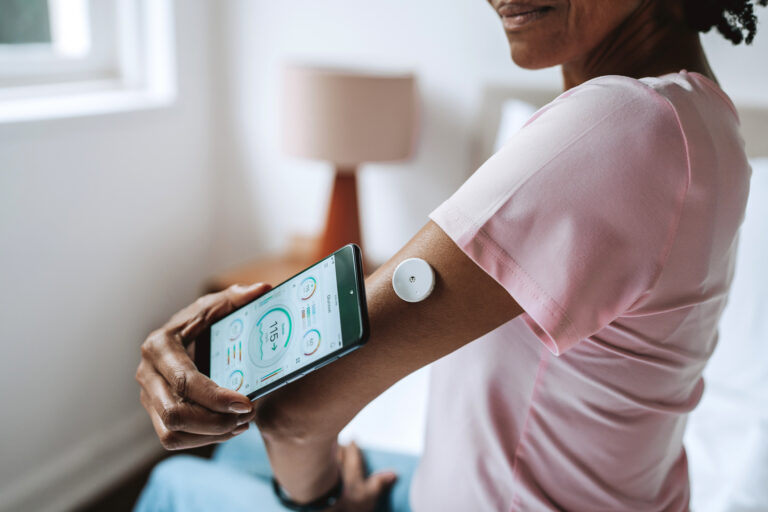Close-Up of Senior Black Woman Scanning Glucose Sensor with Smartphone on Bed